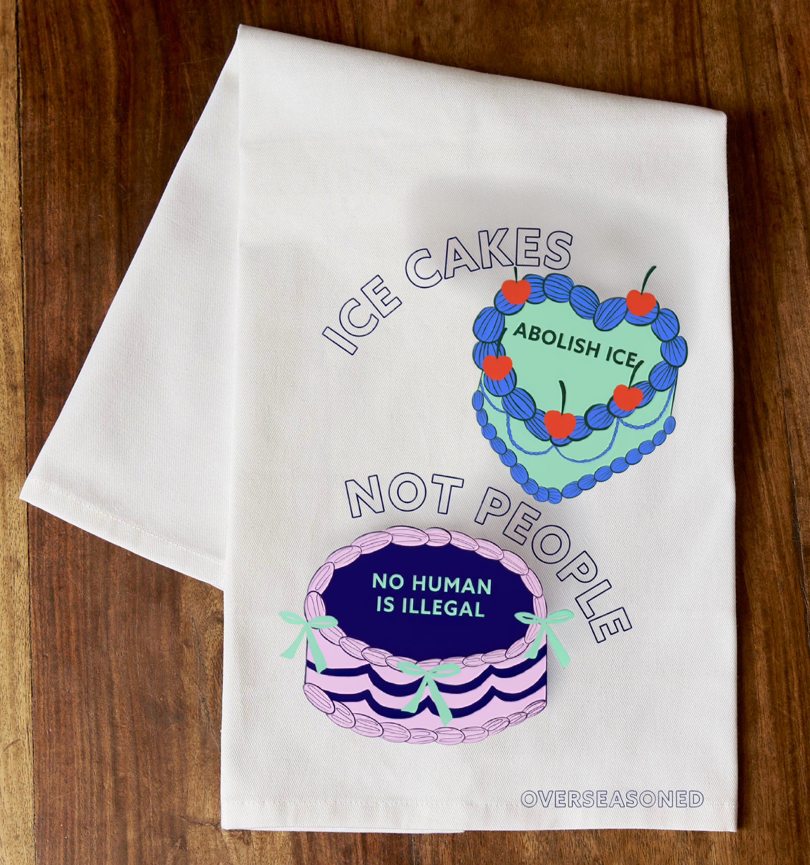 Ice Cakes Not People tea towel mockup on a wooden surface, featuring Abolish ICE and No Human Is Illegal cake designs by Overseasoned